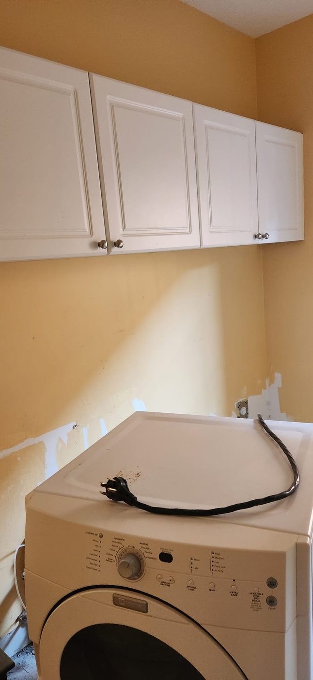 Laundry room before renovation, worn walls and old dryer